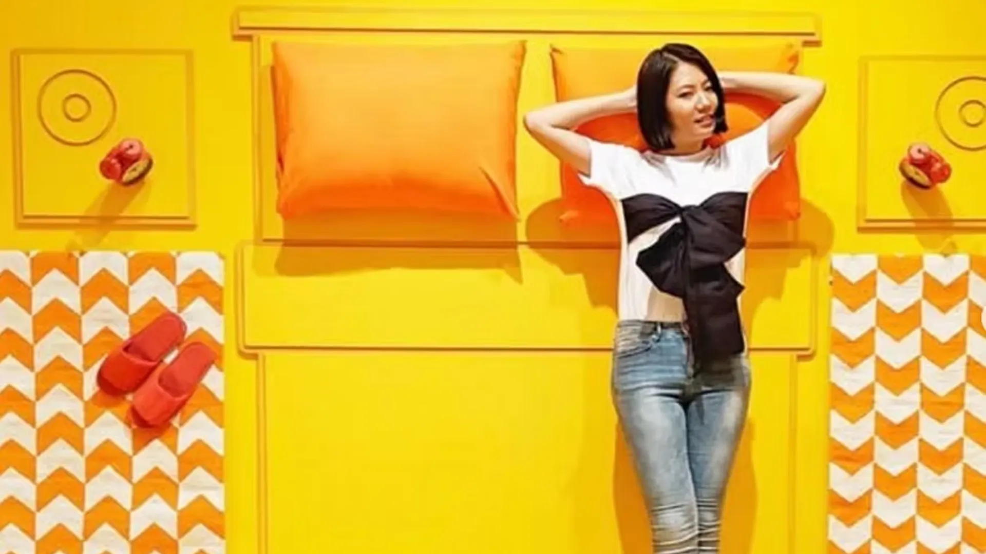 Girl laying on yellow bed with orange pillows.