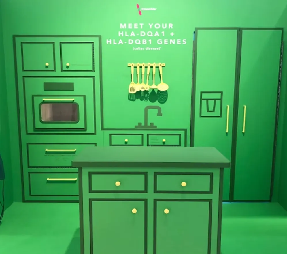 Immersive kitchen-themed installation rendered in a monochromatic green palette, featuring oversized cabinetry, appliances, and interactive elements that translate genetic information into a familiar domestic setting. The vignette transforms a specific genetic marker into a tangible, sensory experience, using environmental storytelling and physical interaction to make complex health insights intuitive, memorable, and easily shareable.